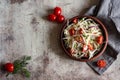 Delicious vegetarian salad with fresh cabbage, tomatoes, herbs, olive oil in a stylish plate on a gray background