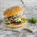 Delicious veggie burger with cabbage, tomato, cucumber, onions and peppers on a light wooden surface Royalty Free Stock Photo