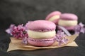 Delicious violet macaron and lilac flowers on black table, closeup