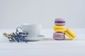 Delicious violet and yellow macarons and cup of latte or americano and branch of fragrant lavender on white wooden