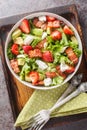 Delicious vitamin salad of strawberries, avocado, bacon, lettuce, feta cheese close-up in a bowl on the table. Vertical top view