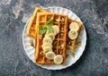 Delicious waffles with banana slices and nuts on grunge background