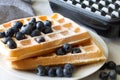 Delicious waffles with blueberries and powdered sugar, waffle maker in background