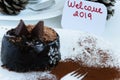 Delicious winter chocolate cake in a plate, a fork cacao decoration and a greeting card `Welcome 2019` Royalty Free Stock Photo