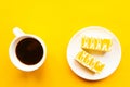 Delicious yellow cakes on a plate and coffee cup, top view. Bright yellow background