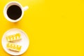 Delicious yellow cakes on a plate and coffee cup, top view. Bright yellow background, minimal concept.