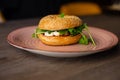 Delicious, yummy sesame donut burger with cheese and greenery filling, sauce served up on pink plate on wooden table Royalty Free Stock Photo