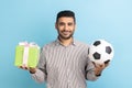 Delighted businessman standing looking smiling at camera, holding soccer ball and present box. Royalty Free Stock Photo