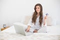 Delighted casual brown haired woman in white pajamas shopping online with her laptop