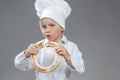 Delighted Caucasian Little Boy Eating Fresh Doughnut Bread Roll. Posing In Cooking Hat