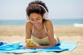 Delighted ethnic female tourist in headphones browsing smartphone on seashore Royalty Free Stock Photo