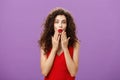 Delighted and excited luxurious adult curly-haired woman with evening makeup in red dress folding lips in amazement Royalty Free Stock Photo