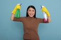 Delighted glad asian housemaid raising arms holding two detergent sprays