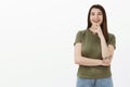 Delighted and happy ambitious young female student with tattoo and brown hair touching chin laughing and smiling pleased