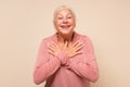 Delighted happy charming old lady with white hair holding palms on heart