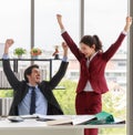 Delighted male and female colleagues smiling and raise hand in air after finishing project in modern office. Teamwork success and