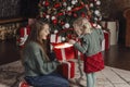 Delighted mother and daughter open a large gift box and look into it. Family evening. Christmas tree on background