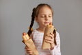 Delighted satisfied little girl with pigtails with hot dog isolated over gray background standing with closed eyes smelling aromat Royalty Free Stock Photo