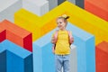 Delighted schoolgirl with backpack against colorful wall