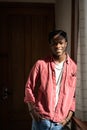 Delighted smiling African American hipster man in pink shirt standing indoors near wooden door