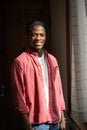 Delighted smiling African American hipster man in pink shirt standing indoors near wooden door