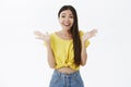 Delighted sweet asian girl with long dark hair in cropped yellow t-shirt clasping hands and smiling touched and joyful