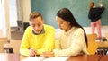 Delighted teenager and Chinese girl schoolmate sitting in classroom, reading notification about approved exams