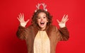 Delighted woman in a Christmas reindeer costume shouts with joy and admiration on colorful red background