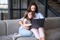 Delighted woman and kid watching video on laptop, sitting on sofa at home Royalty Free Stock Photo