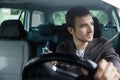 Delighted young man is looking trough the window while driving his car. He is holding his glasses at his right hand. His left hand Royalty Free Stock Photo