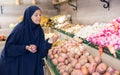 Delighted young Muslim woman purchaser choosing onions in grocery store