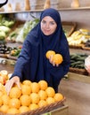 Delighted young Muslim woman purchaser choosing oranges in grocery store