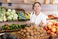 Delighted young woman purchaser choosing kiwi in grocery store