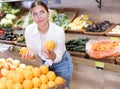 Delighted young woman purchaser choosing oranges in grocery store