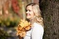 Delightfu blond woman, holding bunch of golden foliage yellow leaves maples in hands near chest, decorate blur. Close up Royalty Free Stock Photo