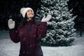 Delightful happy woman having fun, catching snowflakes, standing on a snow covered nature on a snowy cold winter evening