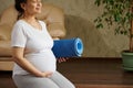 Happy adult pregnant woman sitting in hero pose, touching her belly, enjoying active fitness lifestyle during pregnancy