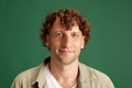 Delightful. Portrait of mature man with curly hair, in casual clothes posing with smile against green studio background