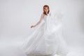 Delightful red-haired bride in a luxurious dress. Light background.