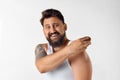 Delightful, smiling, bearded man in singlet taking care after appearance at home against white studio background