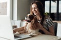 Delightful smiling young woman sitting in kitchen with dog coker spaniel, use laptop. Video call to friends and family