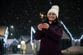Delightful woman lighting sparklers, Bengal lights on a city street, illuminated by garlands on a snowy evening