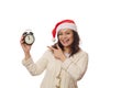 Delightful woman in Santa hat, pointing with her finger on retro alarm clock showing midnight, smiling looking at camera Royalty Free Stock Photo