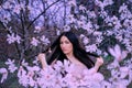A delightful young dark-haired blue-eyed lady stands in the garden of blooming magnolias. hair flies up with her hands
