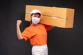 Delivery asian woman or courier wearing an orange masked uniform holds a cardboard box and act strong in the coronavirus concept