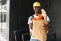 African American courier standing with a package with fresh food from the store.