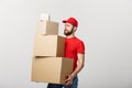 Delivery Concept: Handsome delivery man hold pile cardboard boxes on grey background.