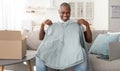 Delivery concept. Happy mature african american man unpacking box and holding new shirt, sitting on sofa Royalty Free Stock Photo