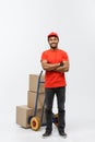 Delivery Concept - Portrait of Handsome African American delivery man or courier pushing hand truck with stack of boxes Royalty Free Stock Photo