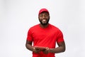 Delivery Concept - Portrait of Happy African American delivery man in red cloth holding a box package. Isolated on Grey Royalty Free Stock Photo